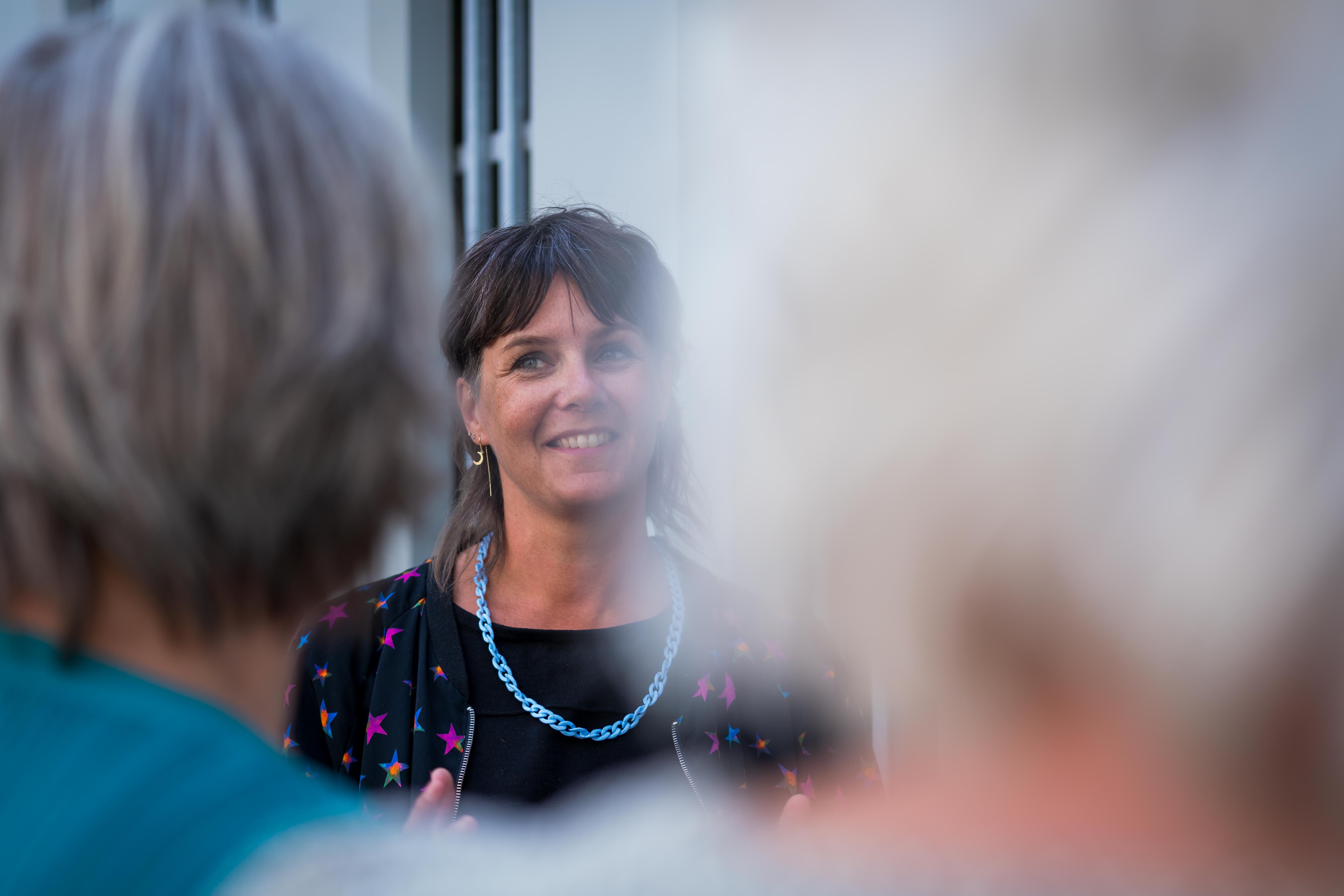 Saskia met blauwe ketting in close up pratend met twee dames